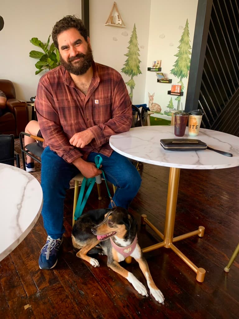 Jon McEwen at a café table, his dog lying at his feet.
